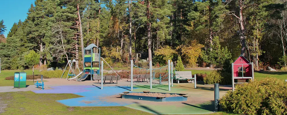 Foto på en lekplats där man ser sandlåda, klätterställning och gungor. 